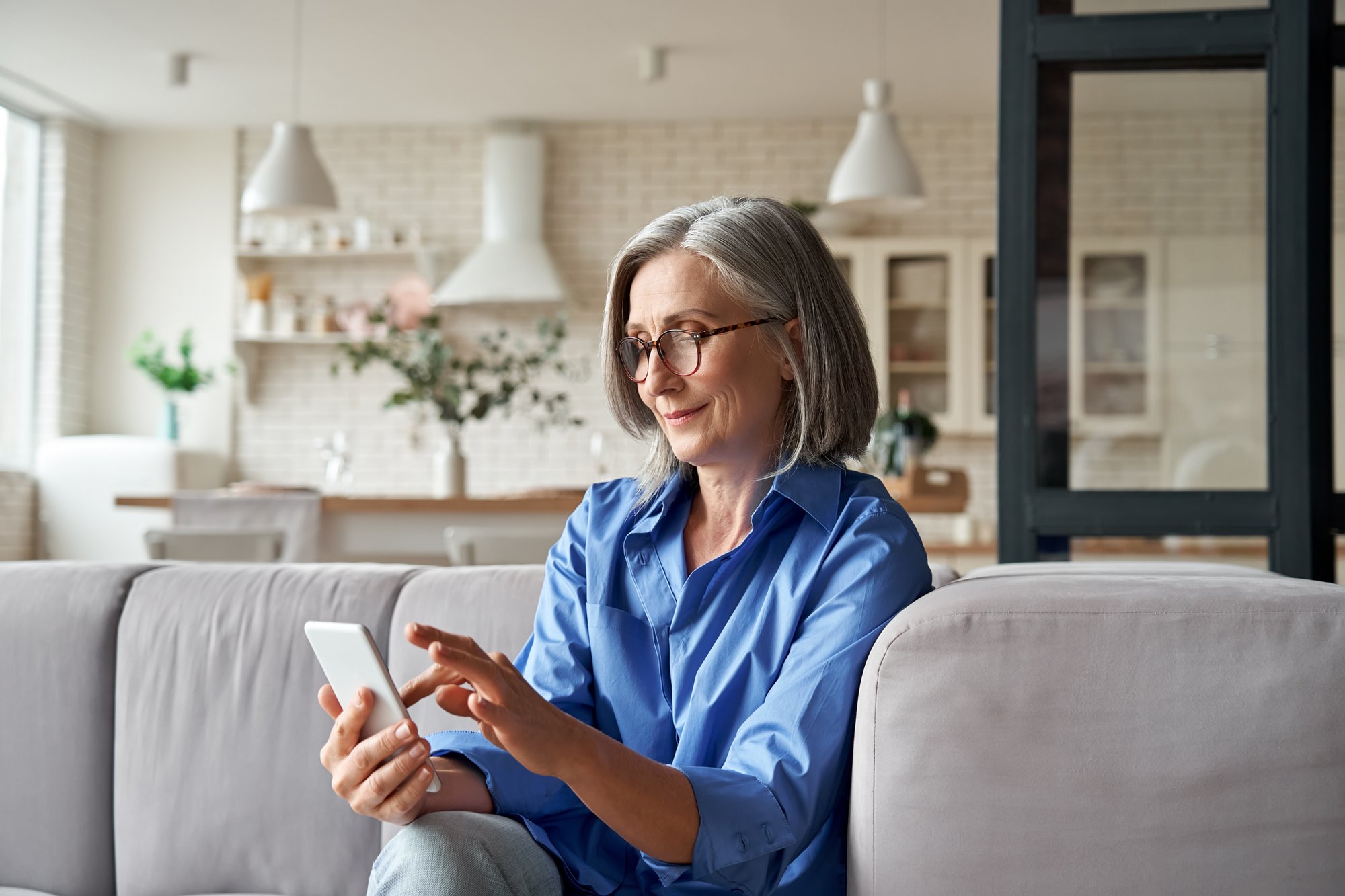 Woman sitting on her sofa filing a home insurance claim on her phone