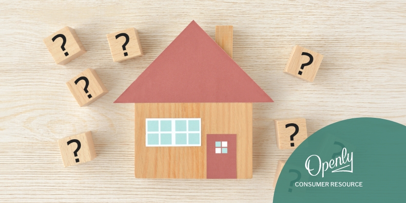 A toy house is surrounded by wooden blocks with question marks on them.