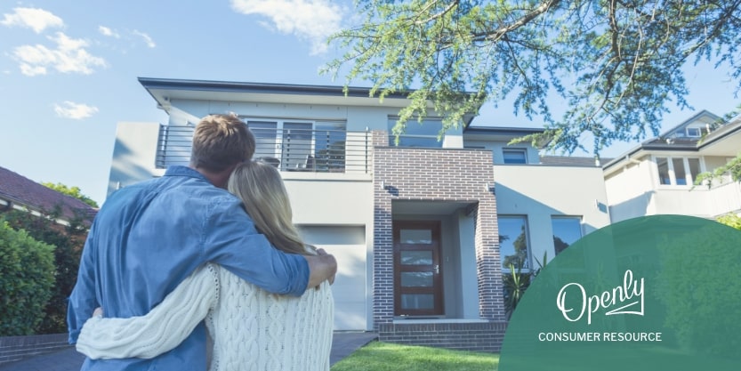 A couple embraces while standing in a driveway looking at a house.