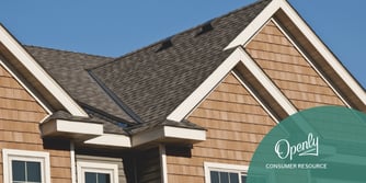 The dark grey shingled roof of a tan house. 