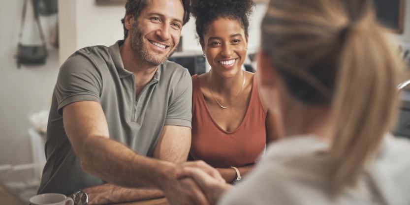 A smiling man and woman shake hands with a woman. 
