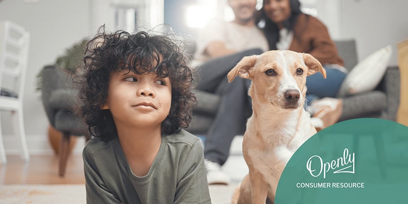 A boy and a dog lay on the floor while a man and woman sit on the couch behind them, smiling.