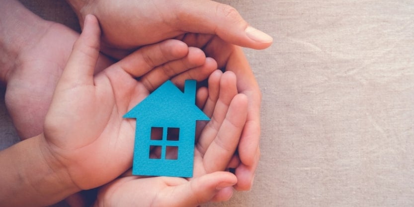 A child's hands, held within an adult's hands, hold a toy house