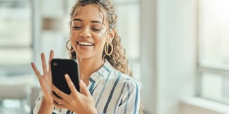 A smiling woman types on her mobile device.