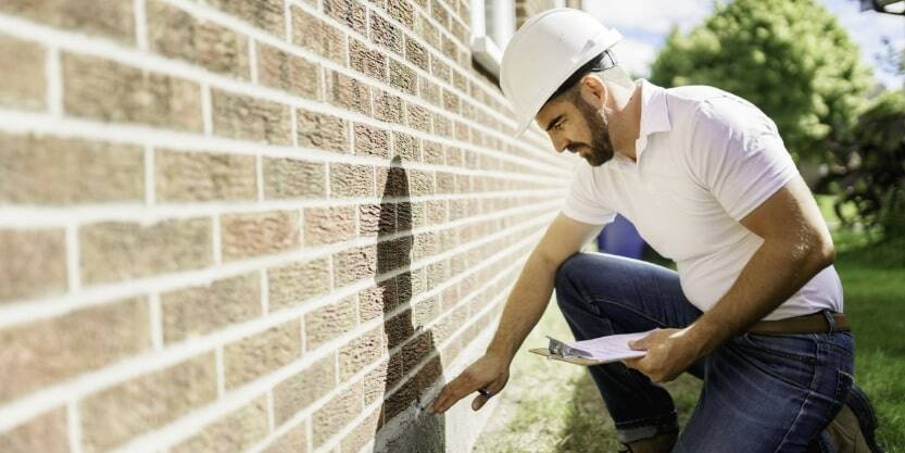 A man in a hardhat inspects foundation damage.
