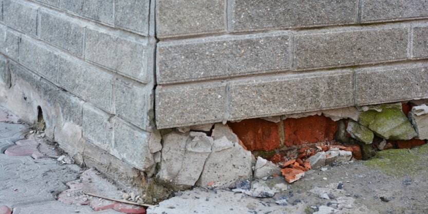 A brick building's foundation is crumbling.