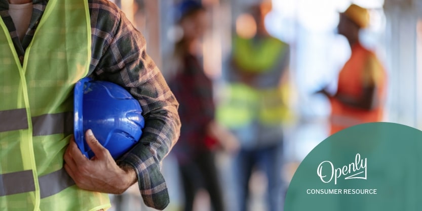 A person holds a hard hat in their arms on a construction site. 