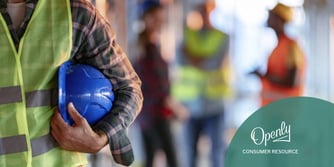 A person holds a hard hat in their arms on a construction site. 