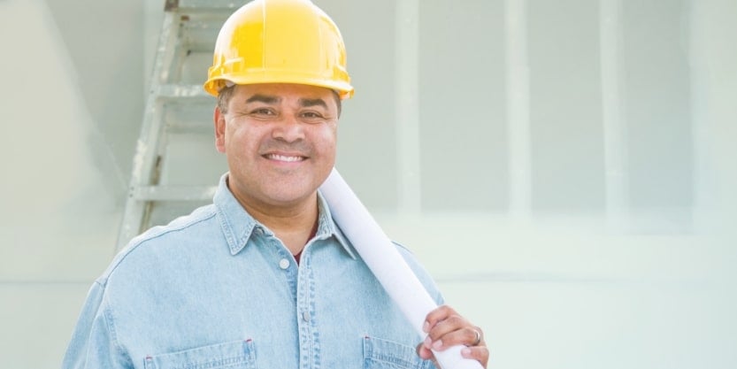 A smiling man wearing a hardhat hold a pipe.