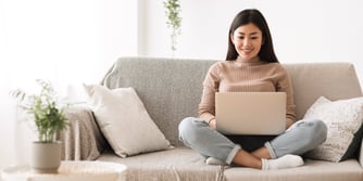  A woman sits on a couch with a laptop in her lap. 