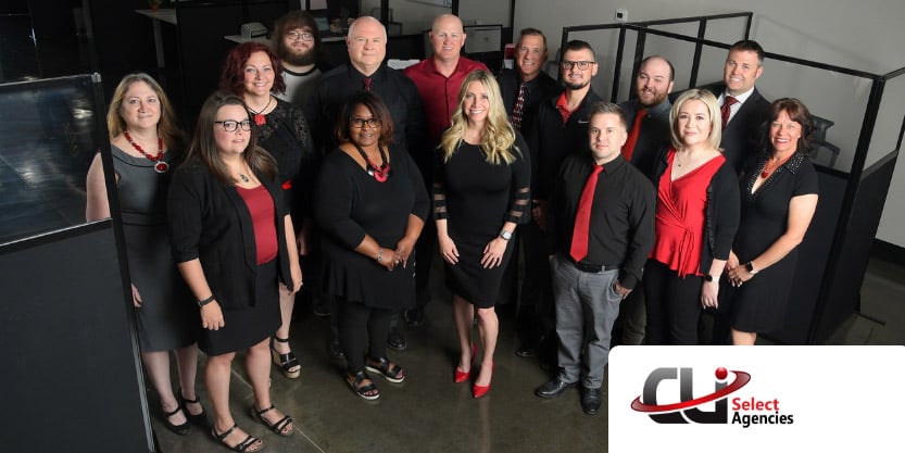 14 people stand in an office and smile at the camera. 
