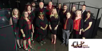 14 people stand in an office and smile at the camera. 