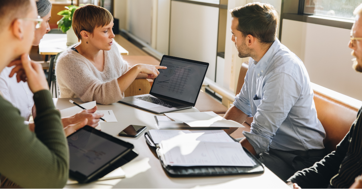 Five people sit at a conference table and look at data on a computer screen.