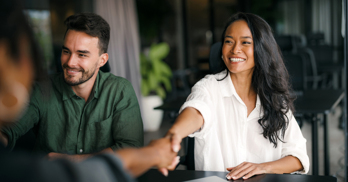 A smiling man and a smiling woman shake hands with two business people. 