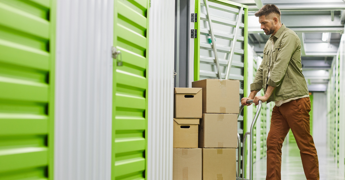 A man uses a car to push a stack of boxes into a storage unit. 